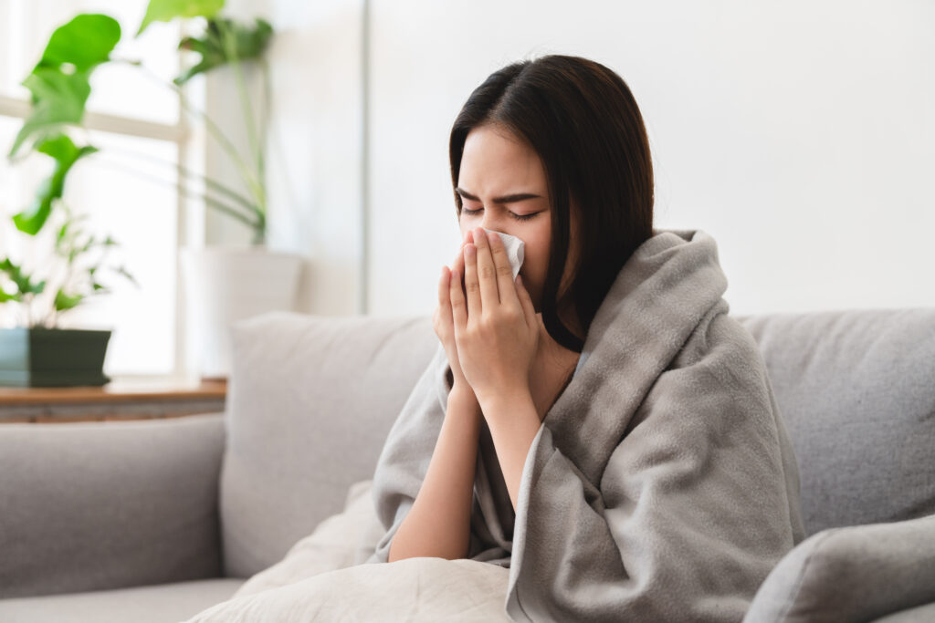 sick woman with a blanket on blowing her nose into a tissue